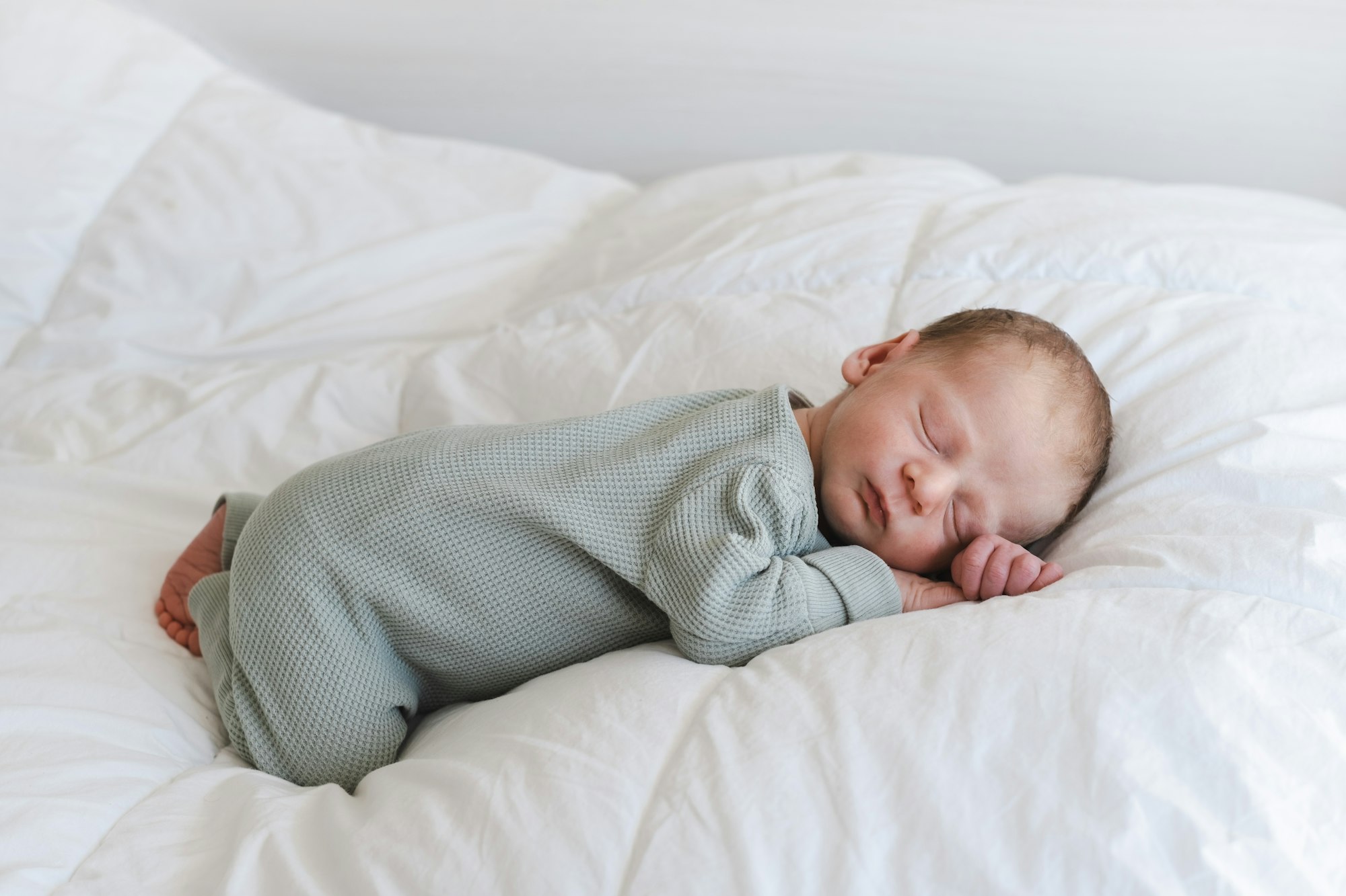 Cute caucasian several days old newborn sleeping on stomach on white blanket at home